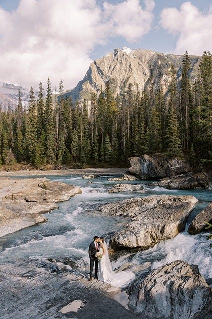 Film wedding photography couple standing in river in front of forest and mountains