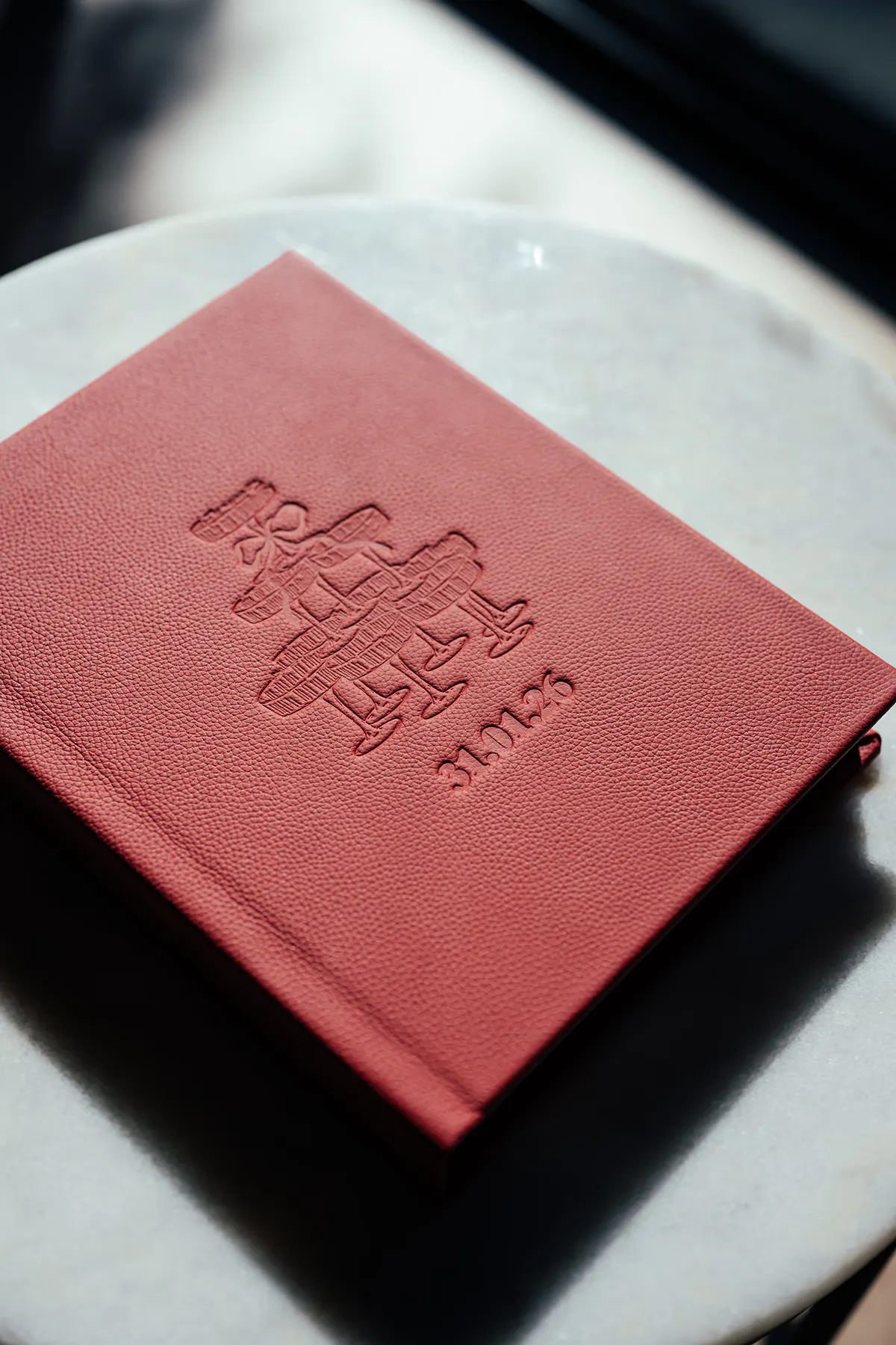 Vision Art red leather wedding album with custom debossed crest illustration and wedding date on a marble surface