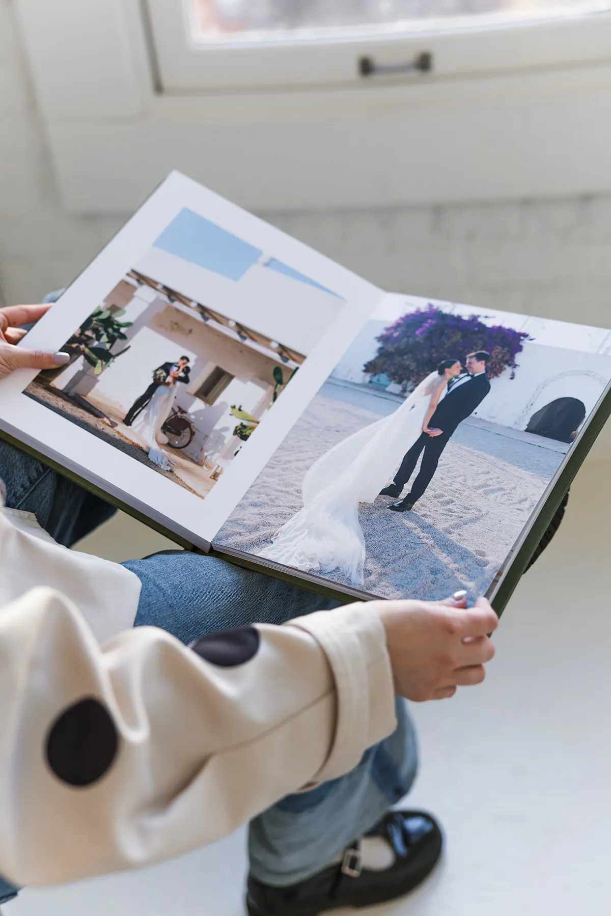 Hands holding an open Vision Art wedding album showing a lay-flat spread of bride and groom destination wedding photos