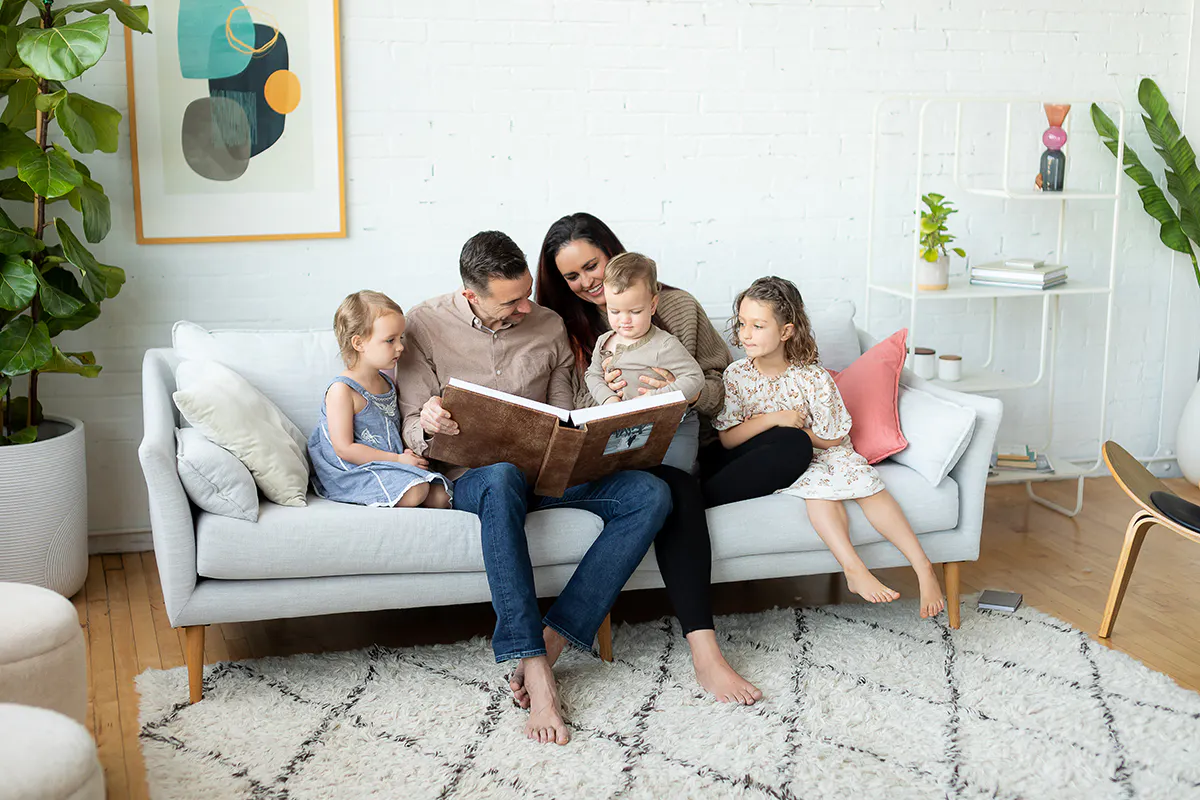 Parents and three children on a sofa looking through a leather Kiss Books album.