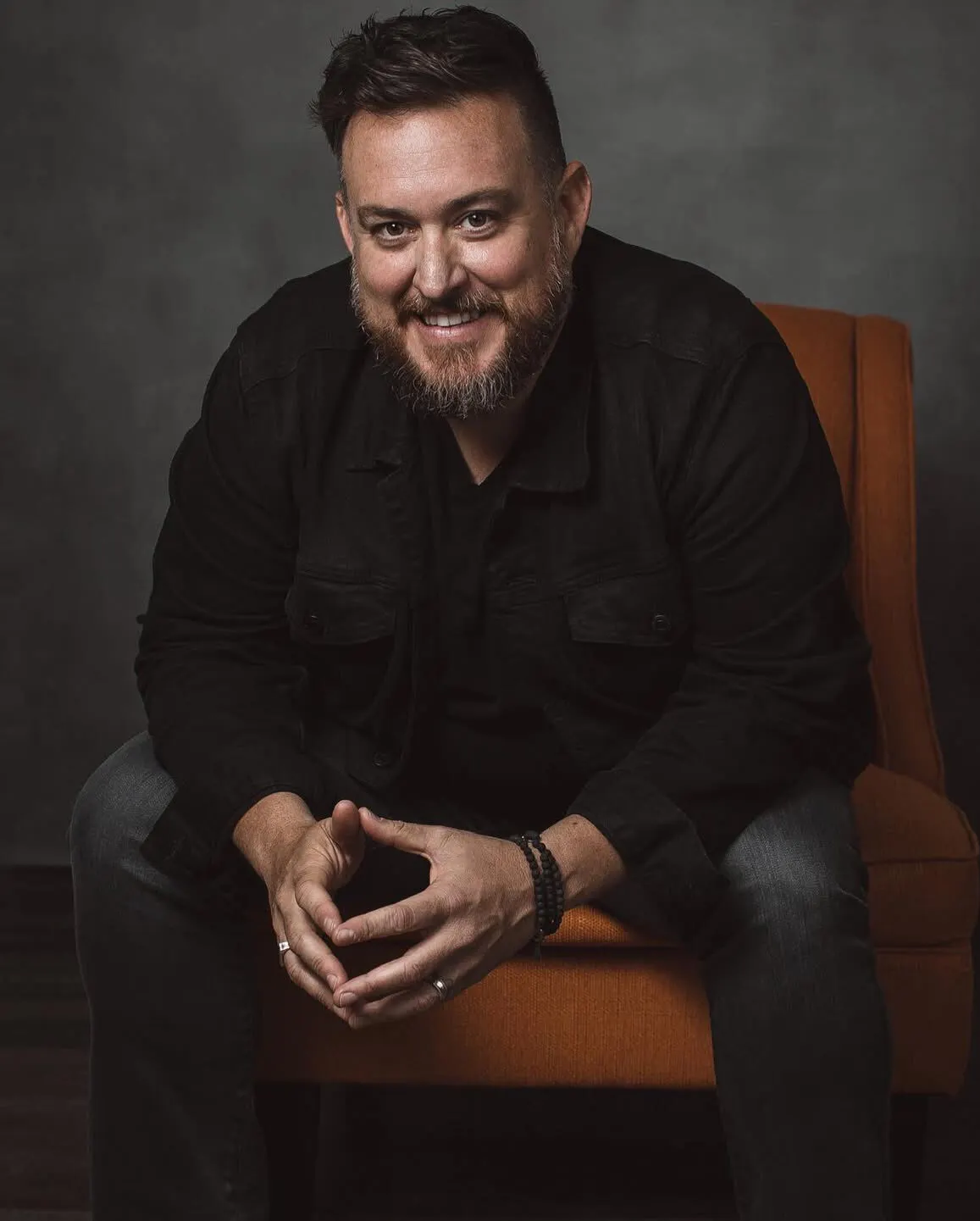 Kiss Books founder Shaun Gordon smiling in a studio portrait on an orange armchair.