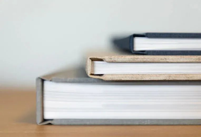 Close-up of three stacked Kiss Books albums showing thick page blocks and fabric covers.