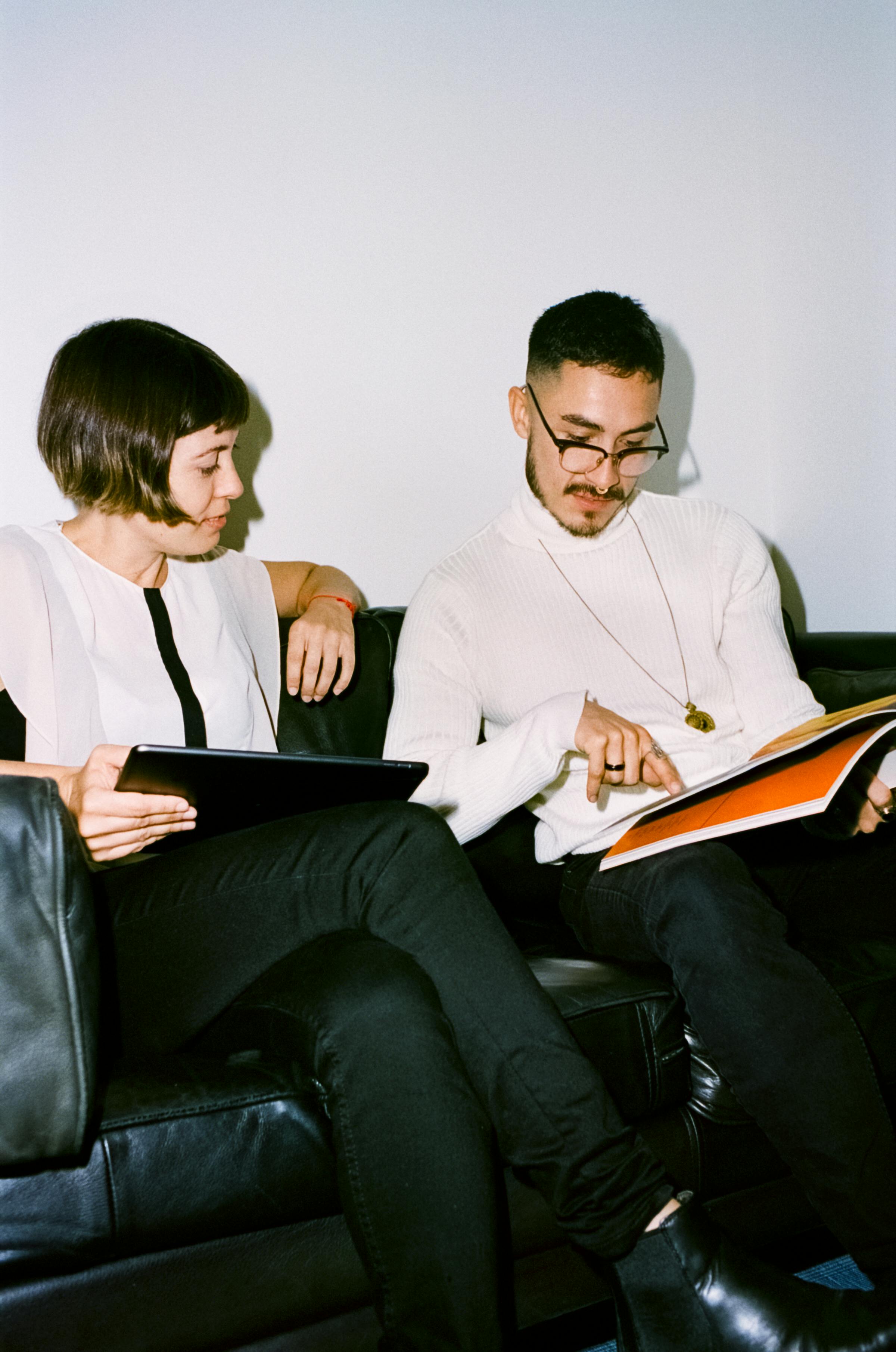 A manager and new hire sit on a couch during an informal 1:1, reviewing a book and tablet together.