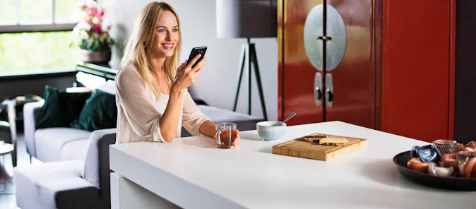 Zittende vrouw in een woonkamer aan het praten tegen haar mobiele telefoon