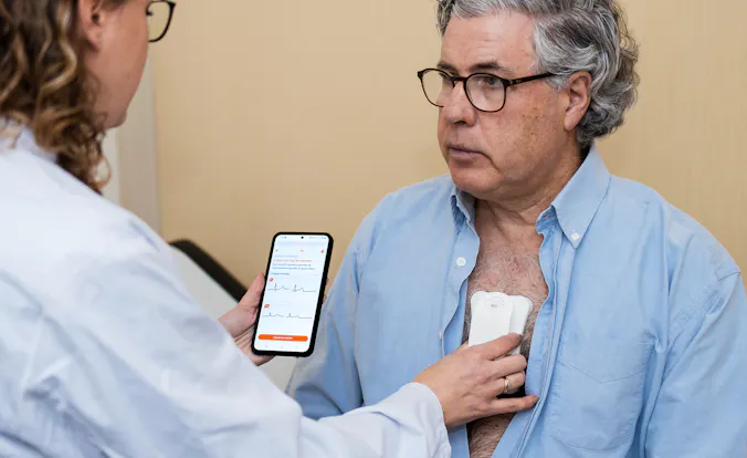 Female doctor holding a heart monitor on the chest of a male patient - Photo: Robbert de Vries, POSITIONE