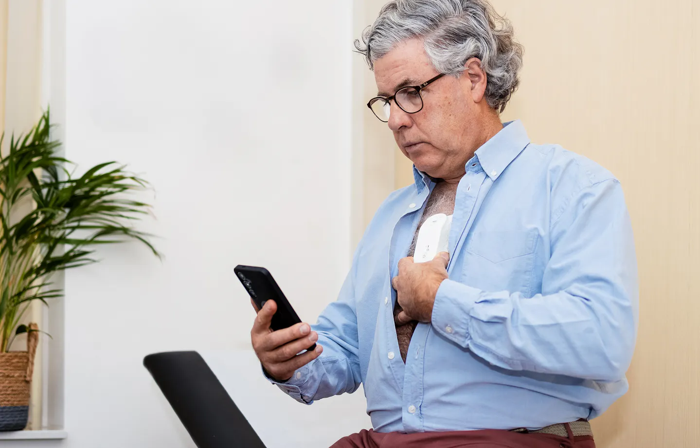 Elderly man with phone in hand and heart monitor on chest - Photo: Robbert de Vries, POSITIONE