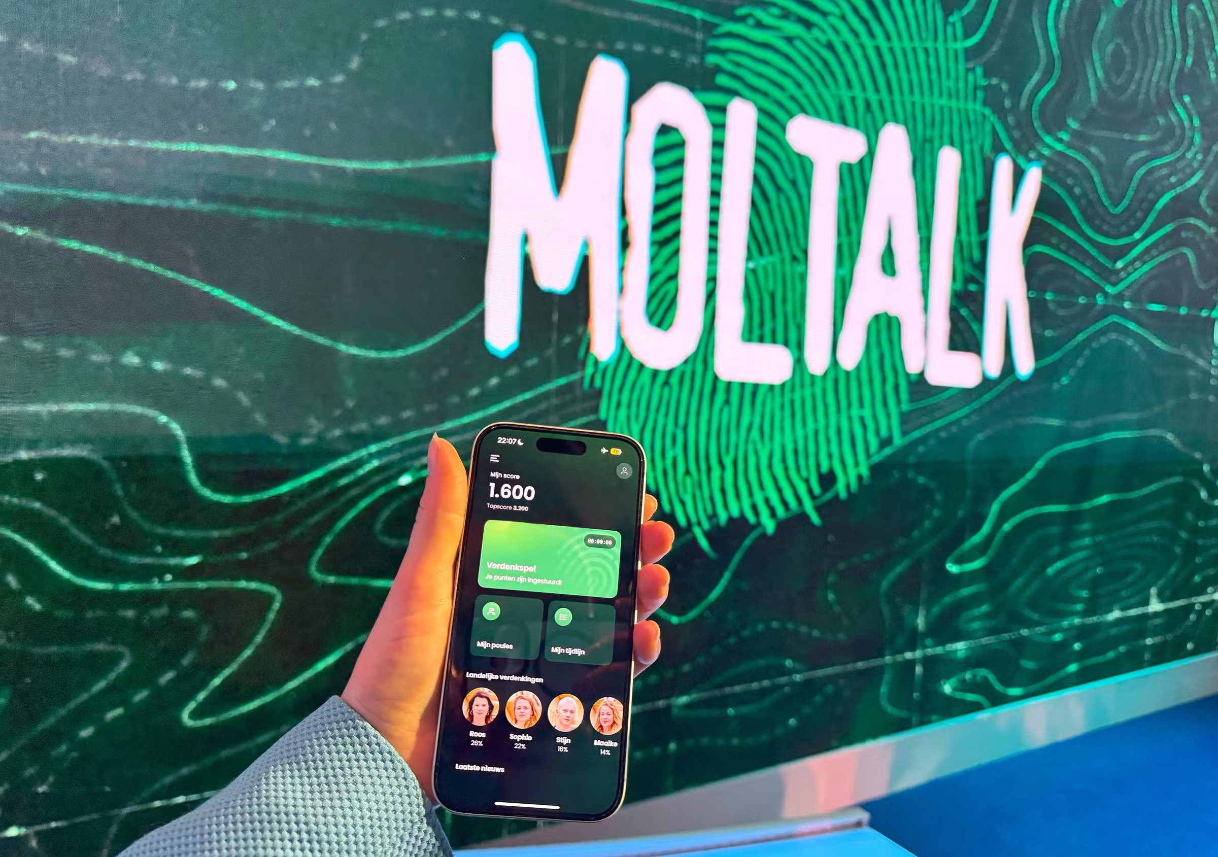 Hand met de app van Wie is de Mol? voor een scherm van tv-programma Moltalk.