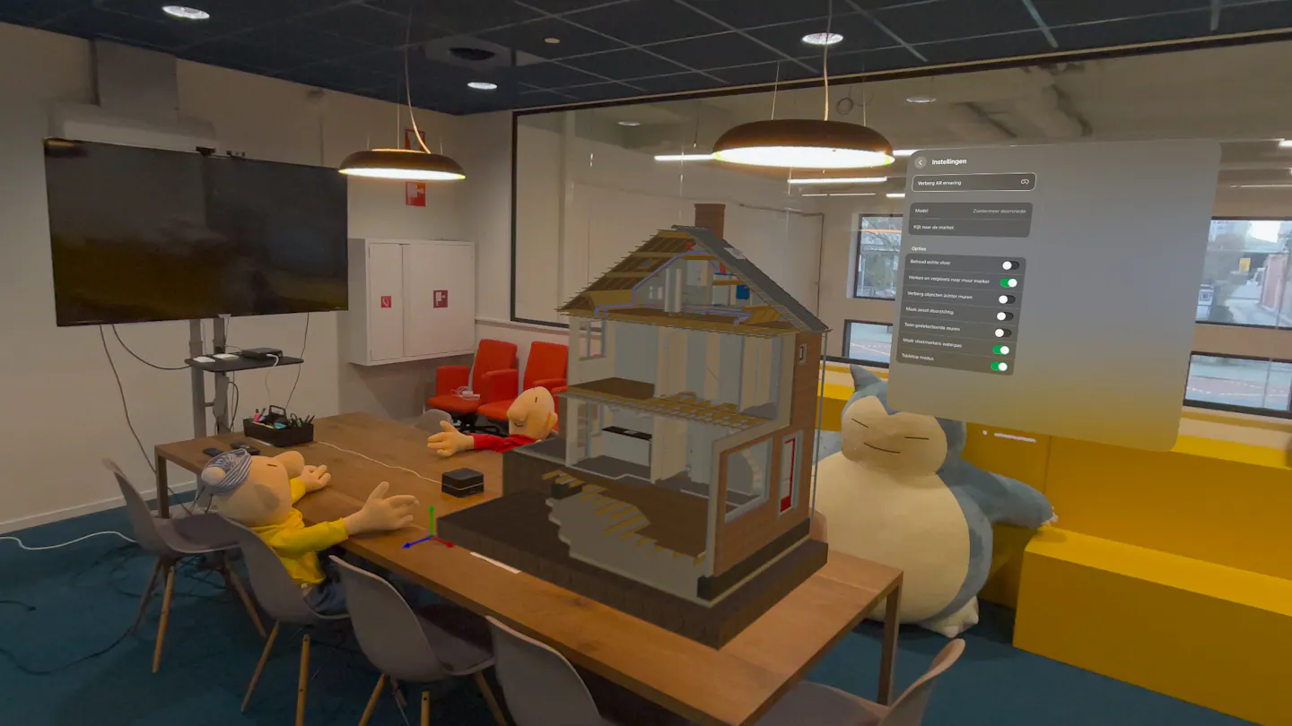 Een vergaderruimte waarin virtueel een huis is geplaatst. Het huis heeft een klein formaat en het menu van de Mark-app is zichtbaar.