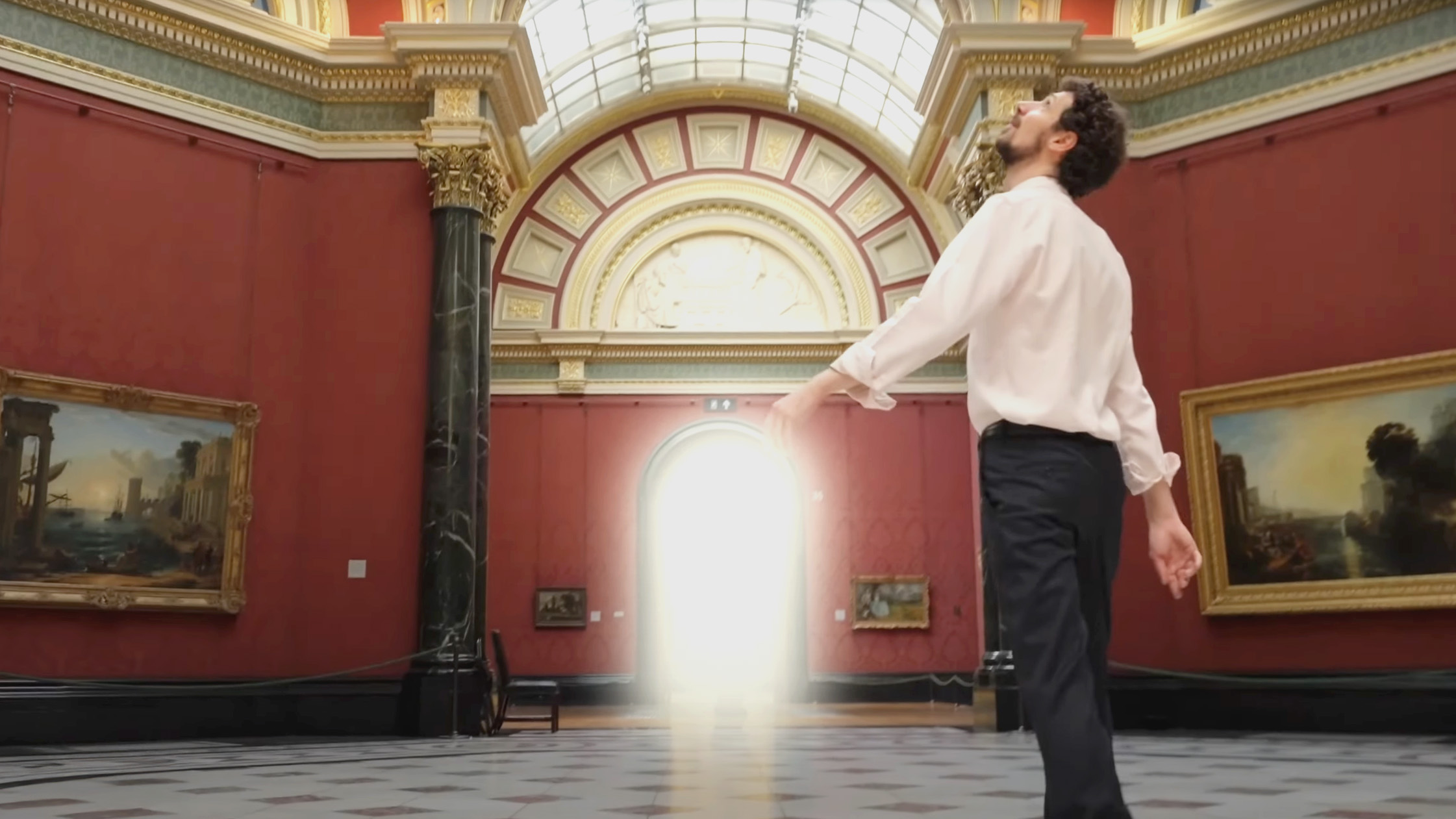 Een man loopt in de rode ruimte van national gallery, genaamd Room 36. Hij kijkt omhoog en de ingang naar een andere ruimte geeft licht. 