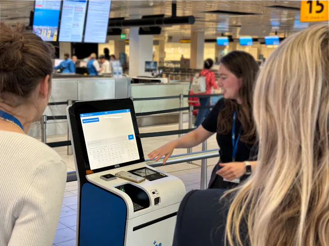 KLM employee explaining to two people at a kiosk at Schiphol.