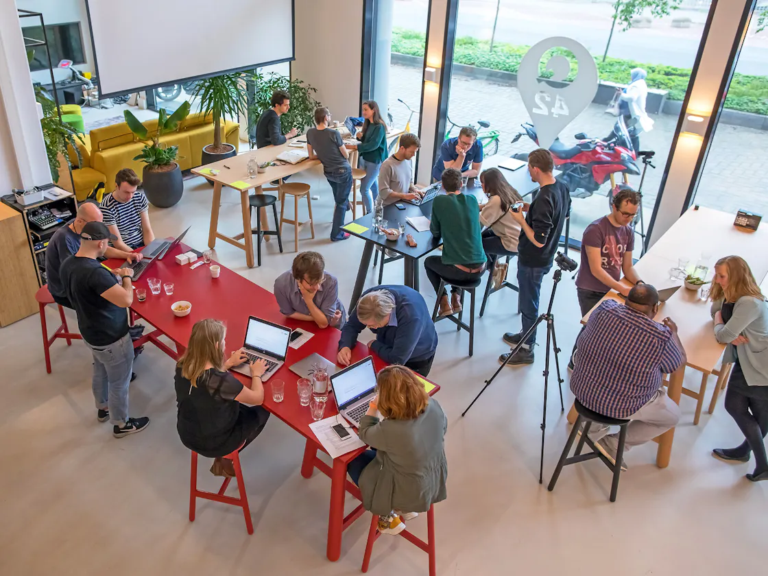 Mensen die staand aan hoge tafels in een ruimte aan een workshop aan het deelnemen zijn.