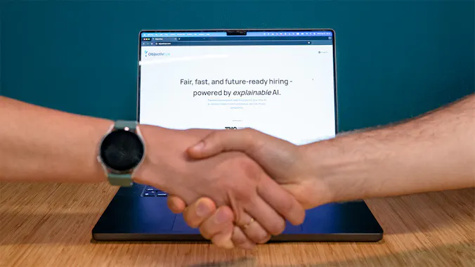 Two people shaking hands in front of a laptop displaying the ObjectivEye website.