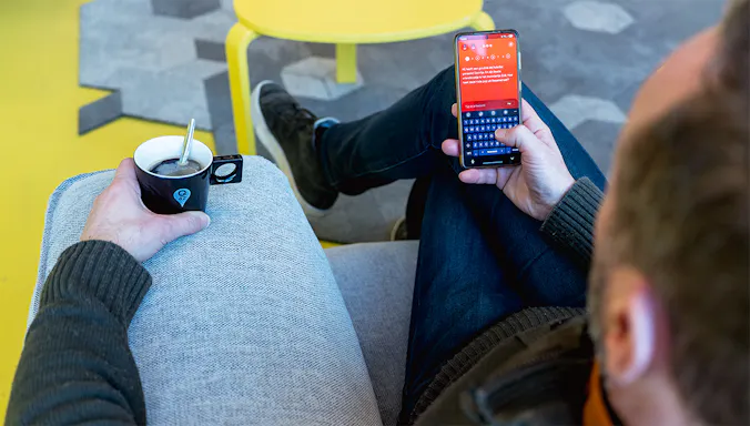 A man holding a cup of coffee and a phone with the app of De slimste mens open.
