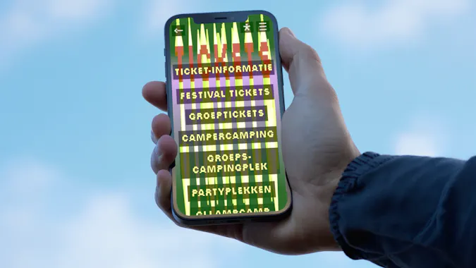 Een telefoon in de lucht, met daarop de ticketinformatie van de Lowlands-website.