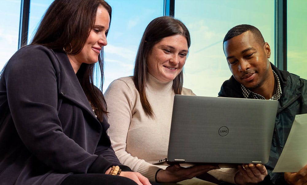 Three coworkers smiling and sharing a laptop