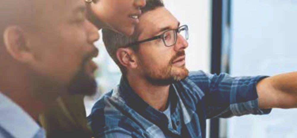 Three people collaborating while looking at a computer screen, discussing work together in an office setting.