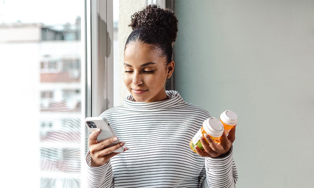 Woman looking at her phone while holding medicine