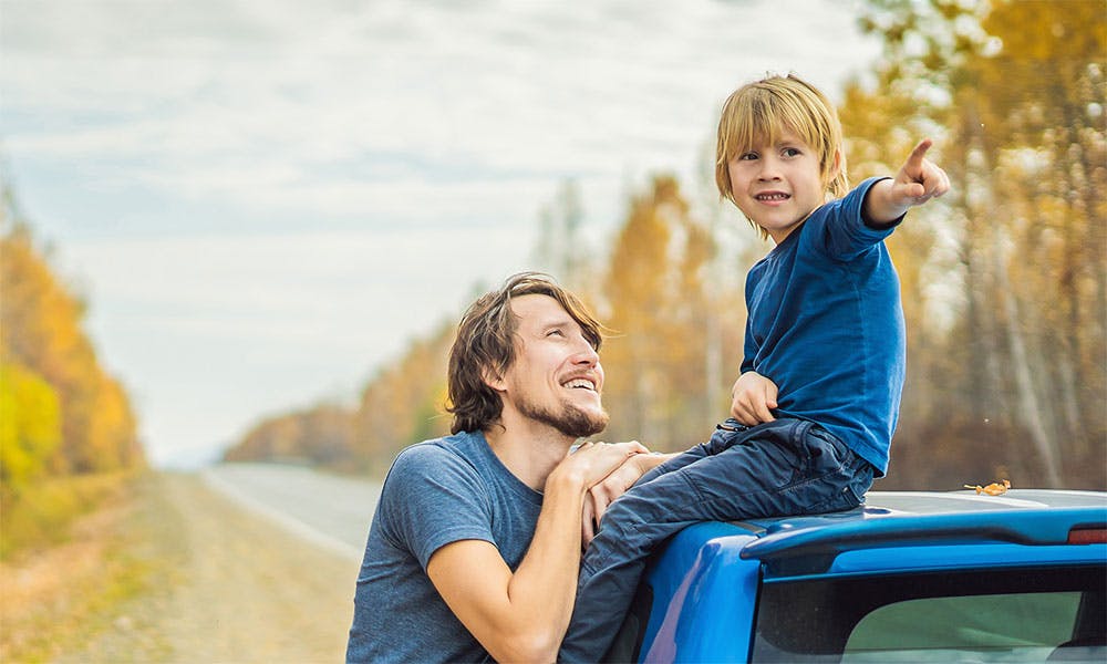 Dad and son on a car, son is pointing in a direction with dad smiling