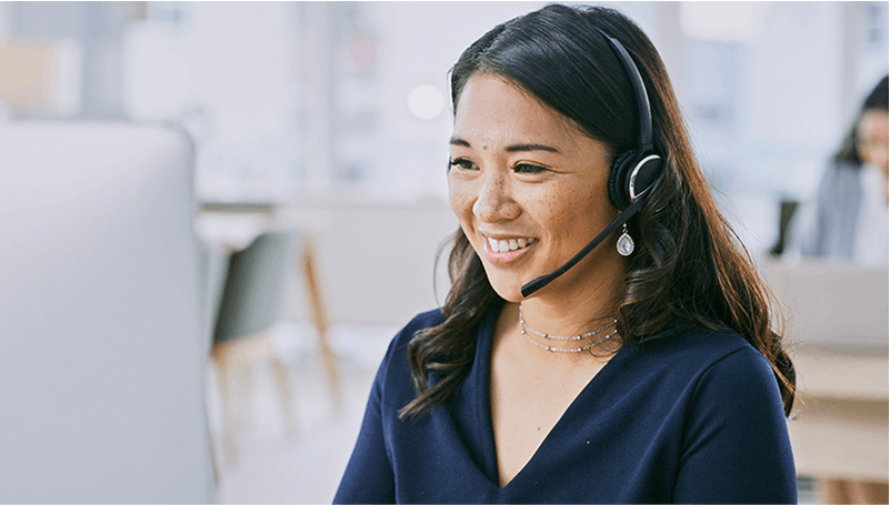 Asian woman using headset in front of a computer smiling