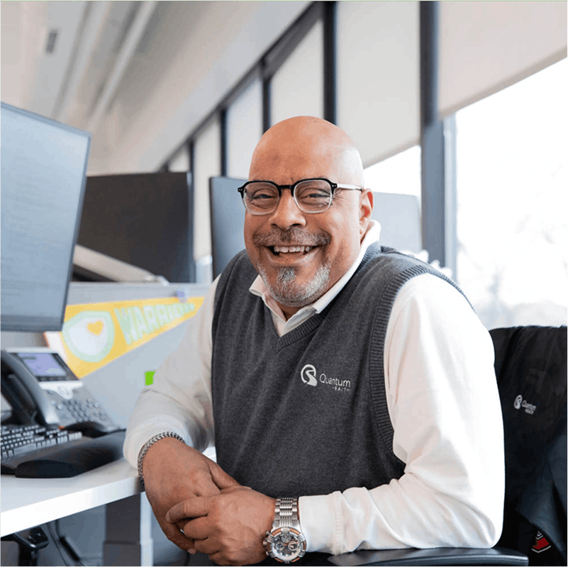 Quantum Health male employee smiling at the camera in front of a computer