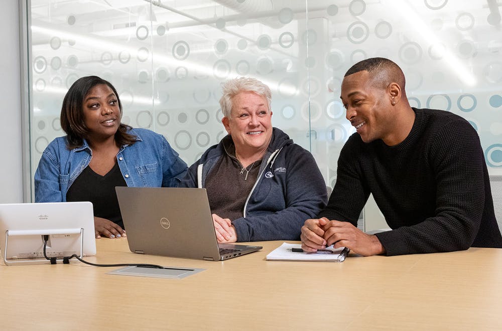 3 employees in a meeting room looking at a laptop