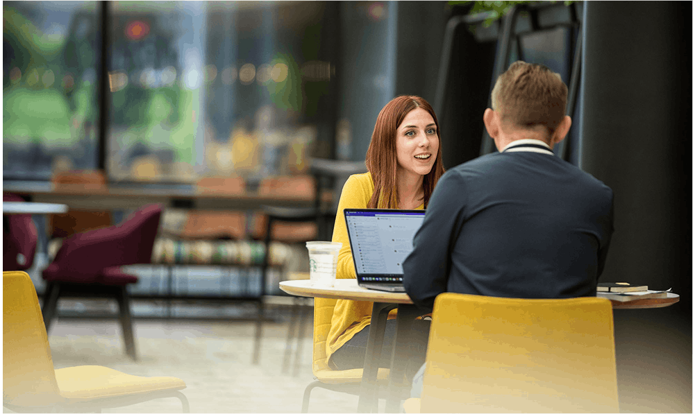 2 QH employees in cafe talking at table