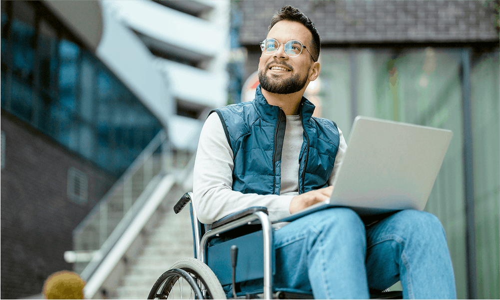 man in wheelchair looking up and smiling with laptop on his lap