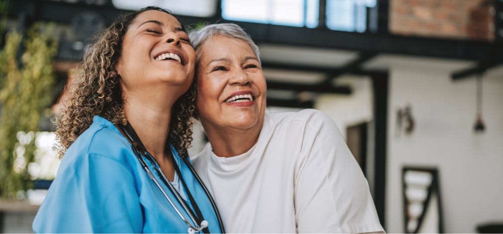Healthcare worker hugging and laughing with elderly woman
