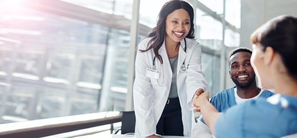 Black female doctor shaking colleague's hand at a table in a business-meeting setting