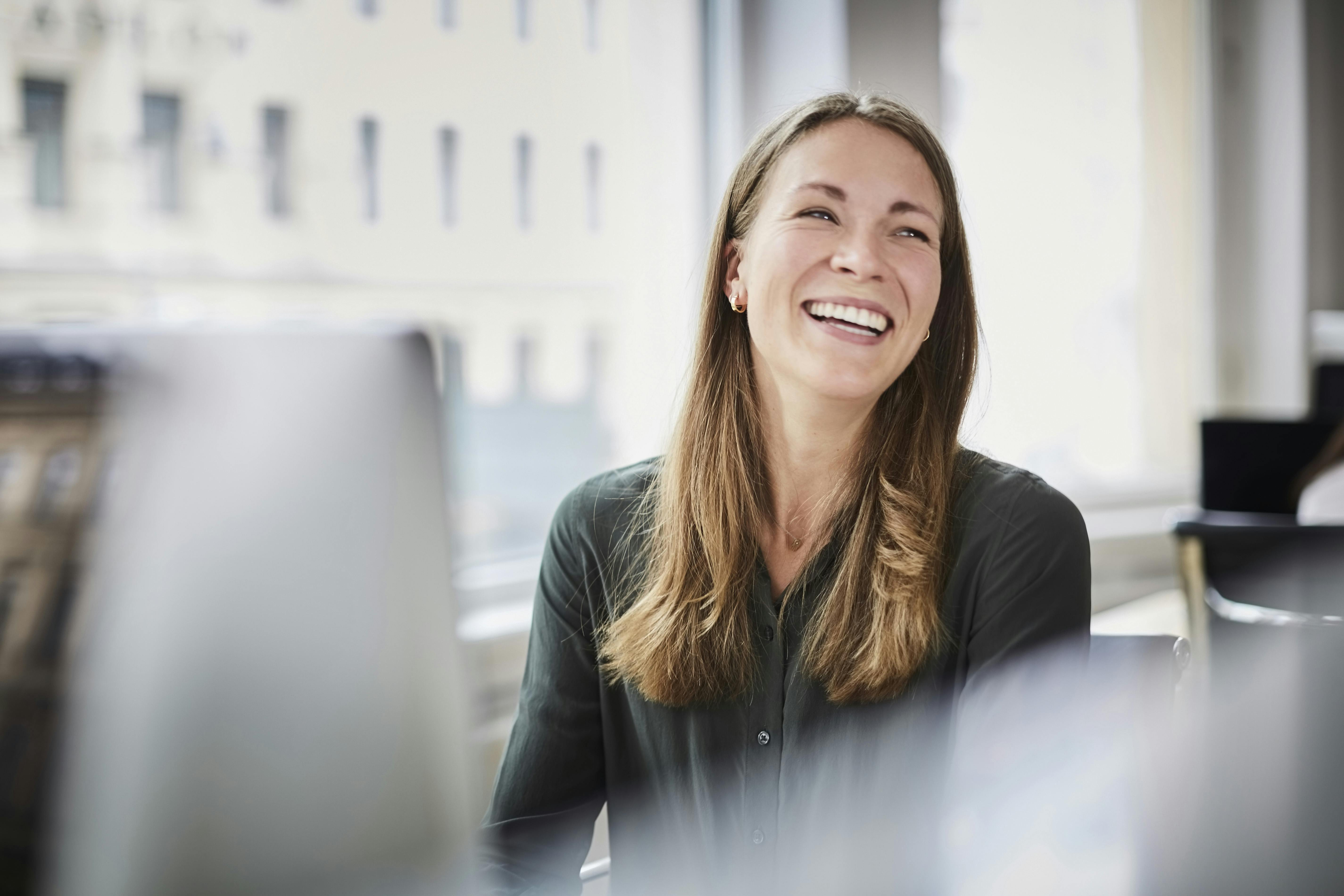 Smiling woman seated in an office workspace, looking slightly to the side.