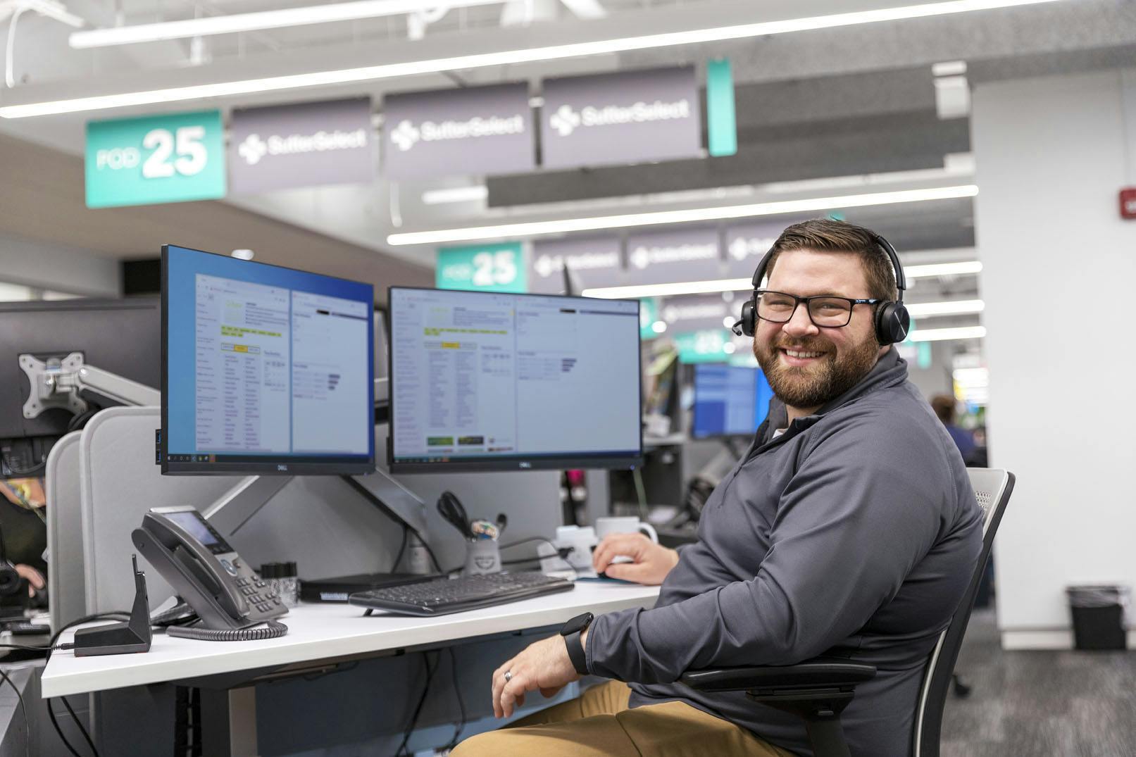 Man with headset smiling in front of computer monitors