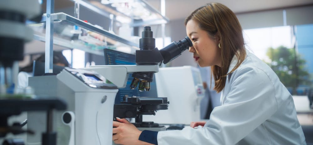 Woman in lab coat looking into microscope