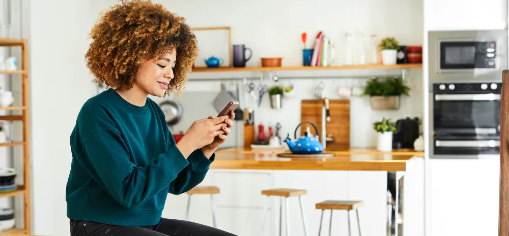 Woman sitting on kitchen counter scrolling on phone