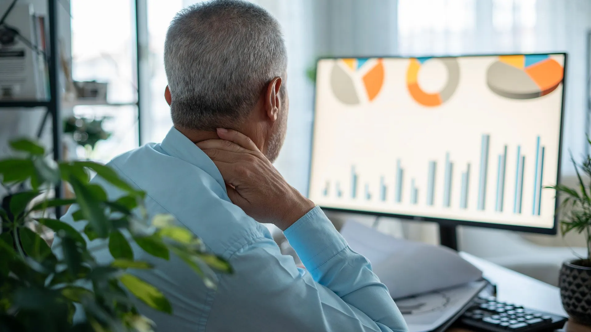 Man looking at a monitor with graphs and holding neck because of pain.