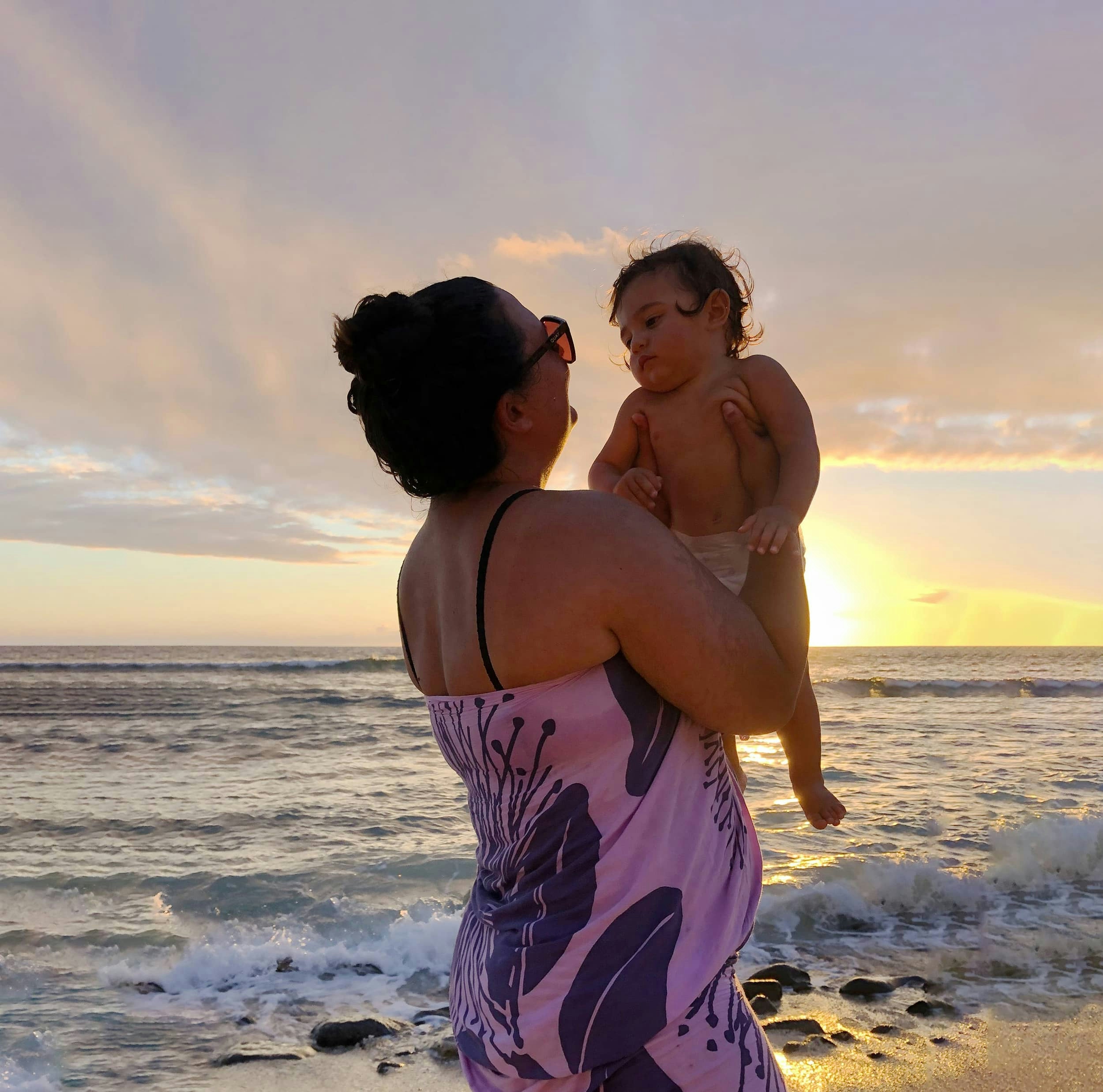 Mother holding baby on the beach during sunset.