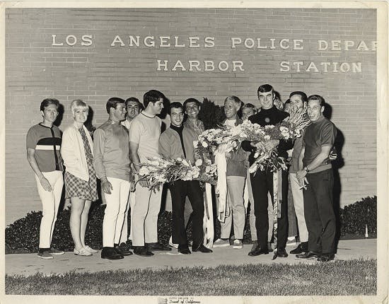 Patrons from The Patch, a gay bar in Wilmington owned at the time by Long Beach resident Lee Glaze, hold bouquets outside the Los Angeles Police Department Harbor Station during the 1968 “flower power” protest against police harassment. Photo courtesy of Lee Glaze.