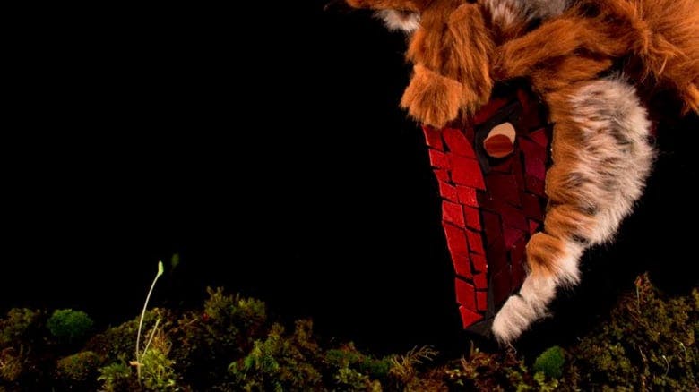 still from H. Kristen Campbell's Swift (2012). Image of a fox made of fur tufts and pieces of felt sniffing at moss at the bottom edge of the image. It's all on a black background