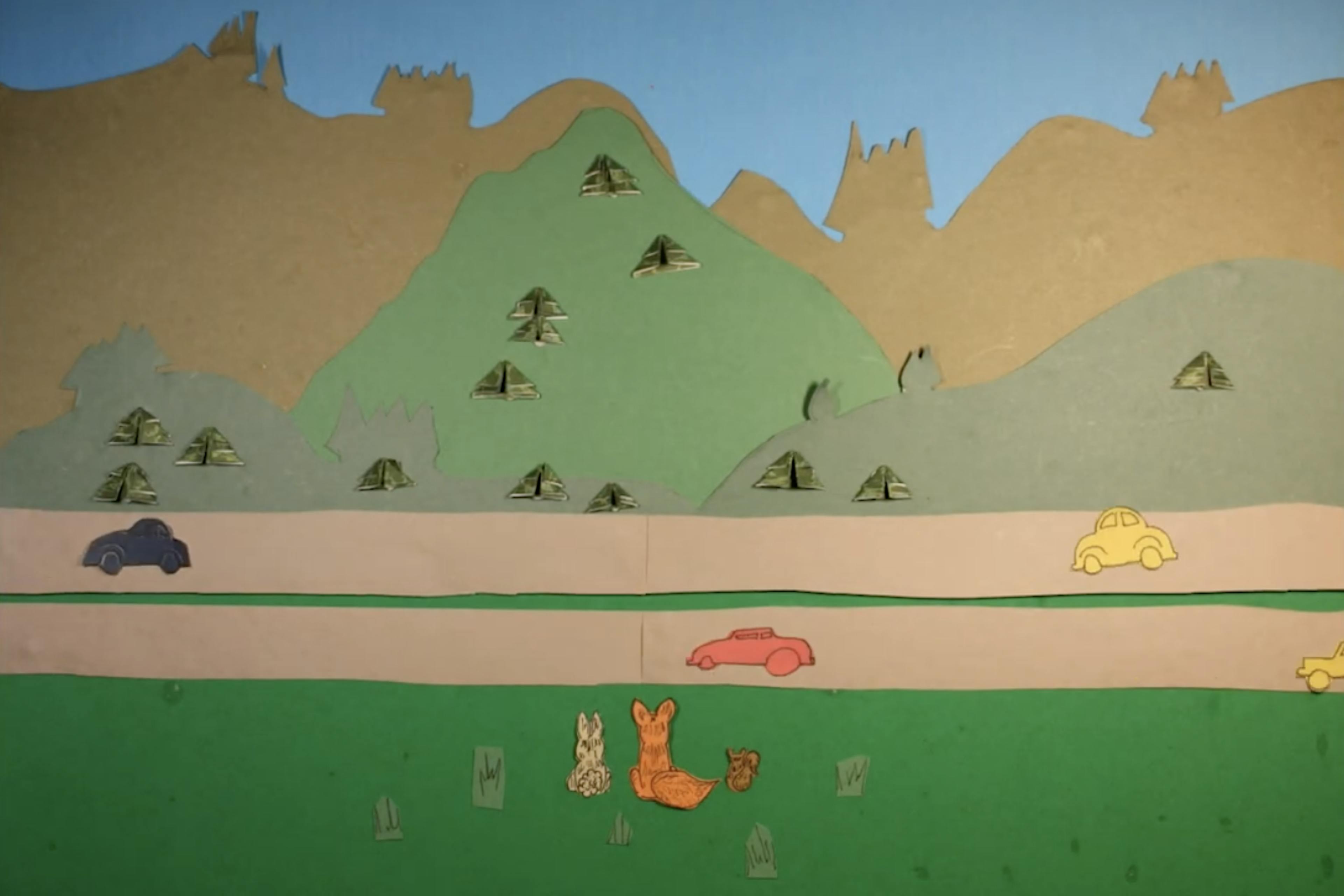 A rabbit, a fox and a squirrel look at a busy highway standing between them and the rolling hills beyond-all made from cut-out construction paper.