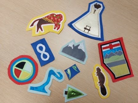 images of flannel cutouts of an Alberta map, the Indigenous four wheel symbol, the rocky mountains, a buffalo, a teepee, and a beaver.