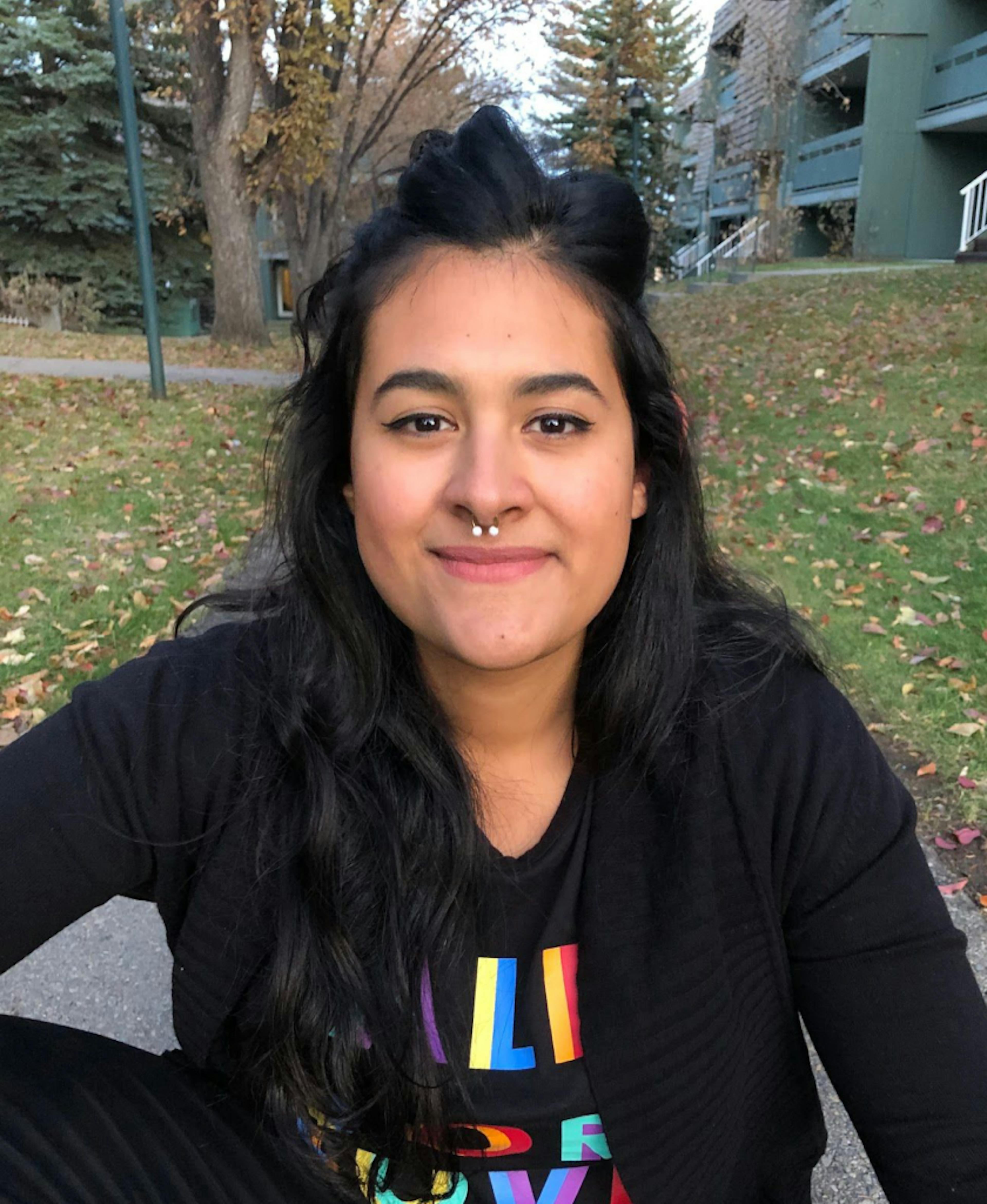 profile picture of Ana Victoria Pinero - 2019-21 CJM Scholarship Winner. She is of Venezuelan decent, with long black hair. She is smiling at the camera. She has brown eyes, a nose ring, and is wearing a black shirt with colourful text on it. 