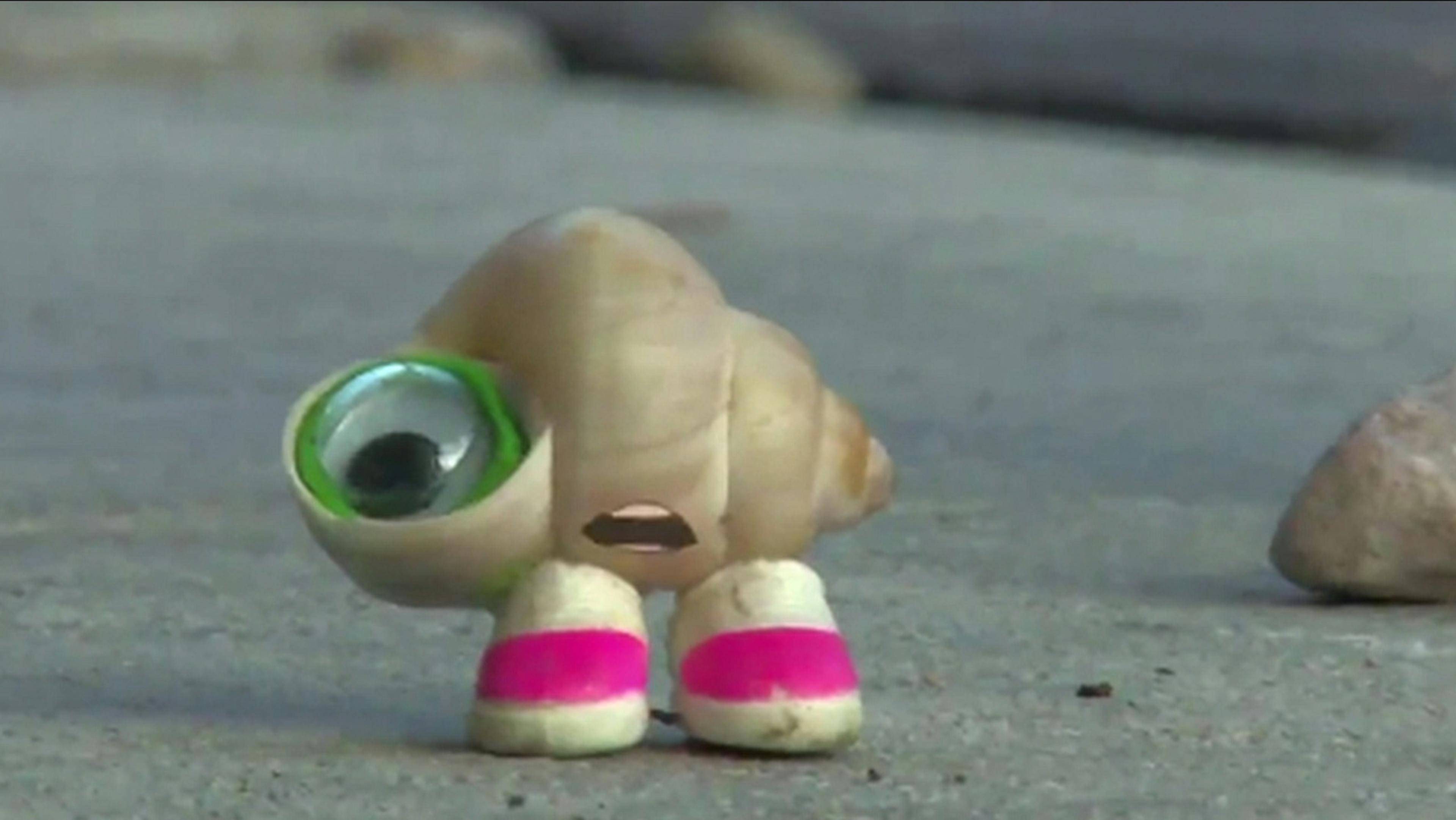 A tiny seashell with a cartoon mouth, googly eye, and white and pink sneakers stands looking shocked