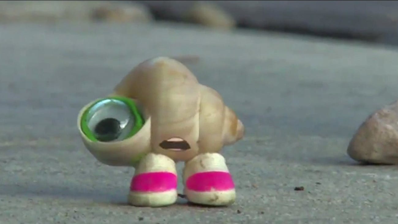 A tiny seashell with a cartoon mouth, googly eye, and white and pink sneakers stands looking shocked