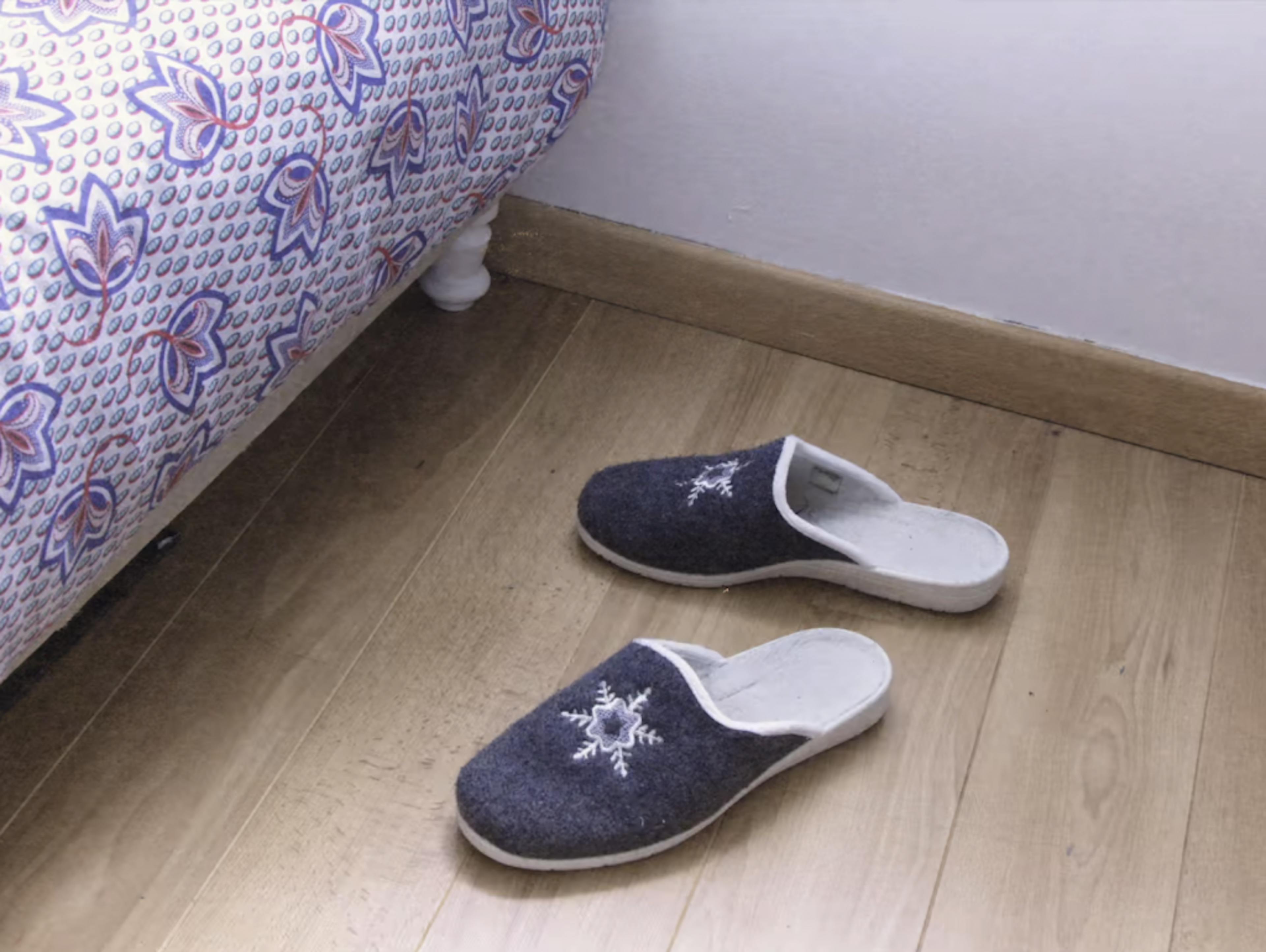 A pair of slippers on the ground beside a bed