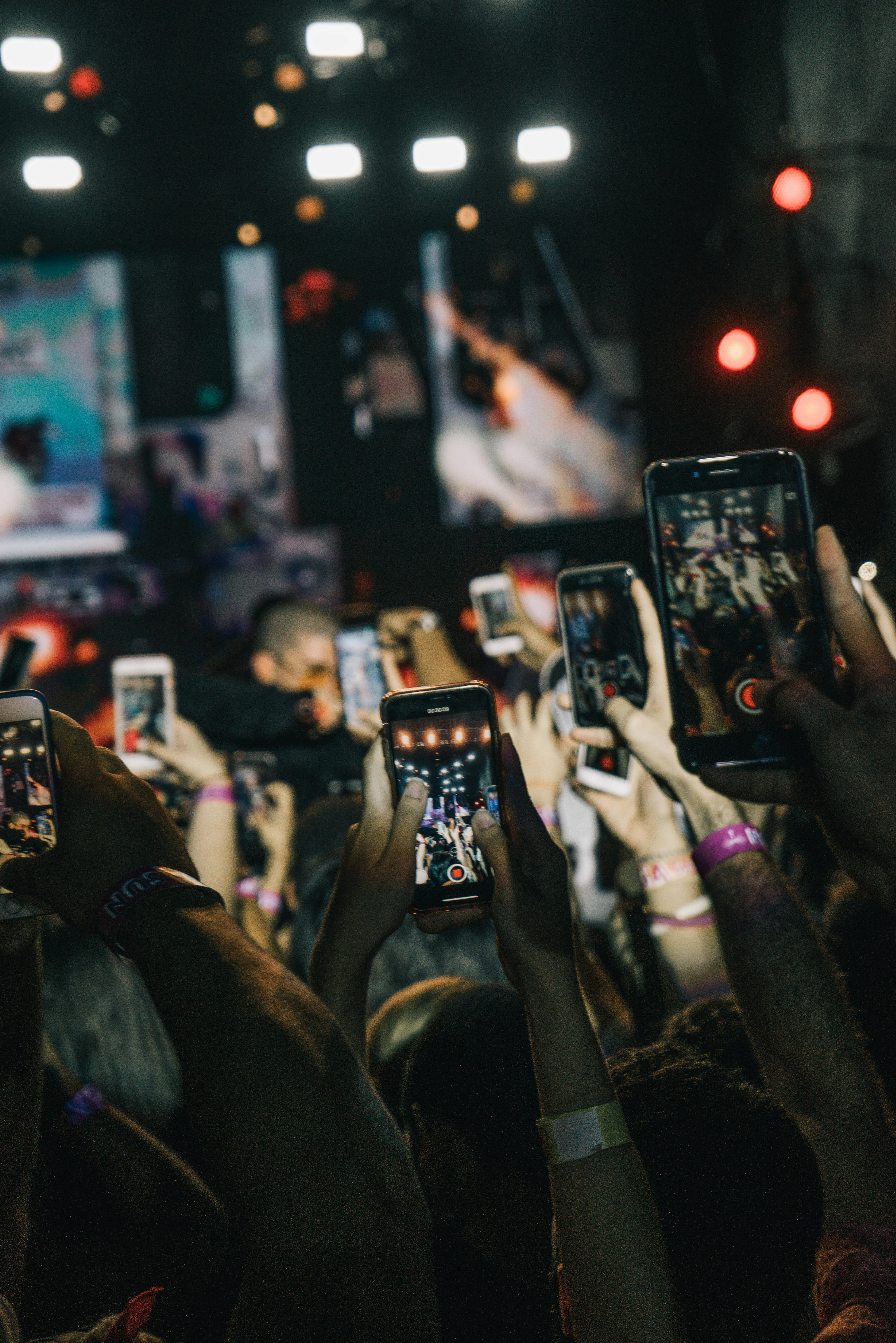 Many people holding multiple phones on their hands, capturing something.  Many lights 
