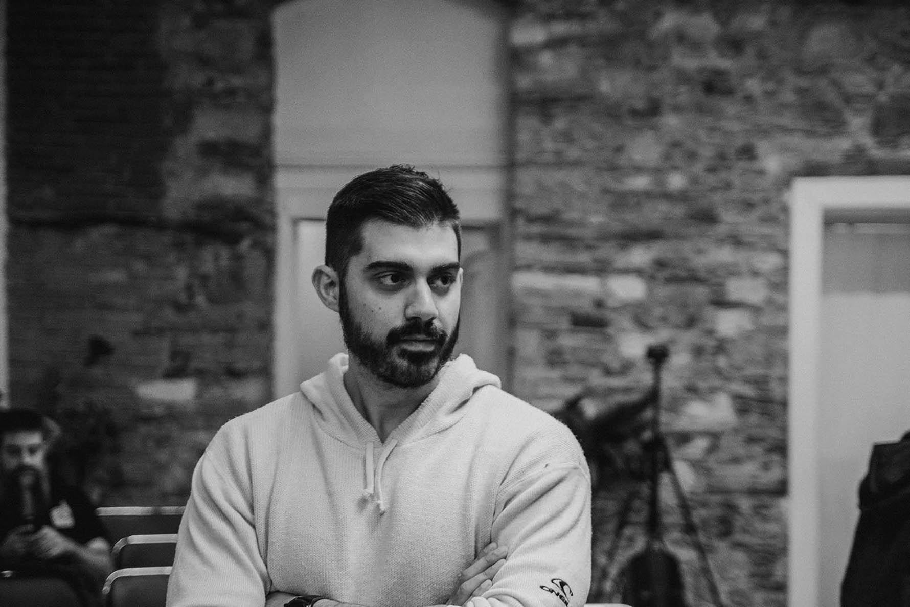 guy with facial dark hair wearing a hoodie looking on his left. Black and white background
