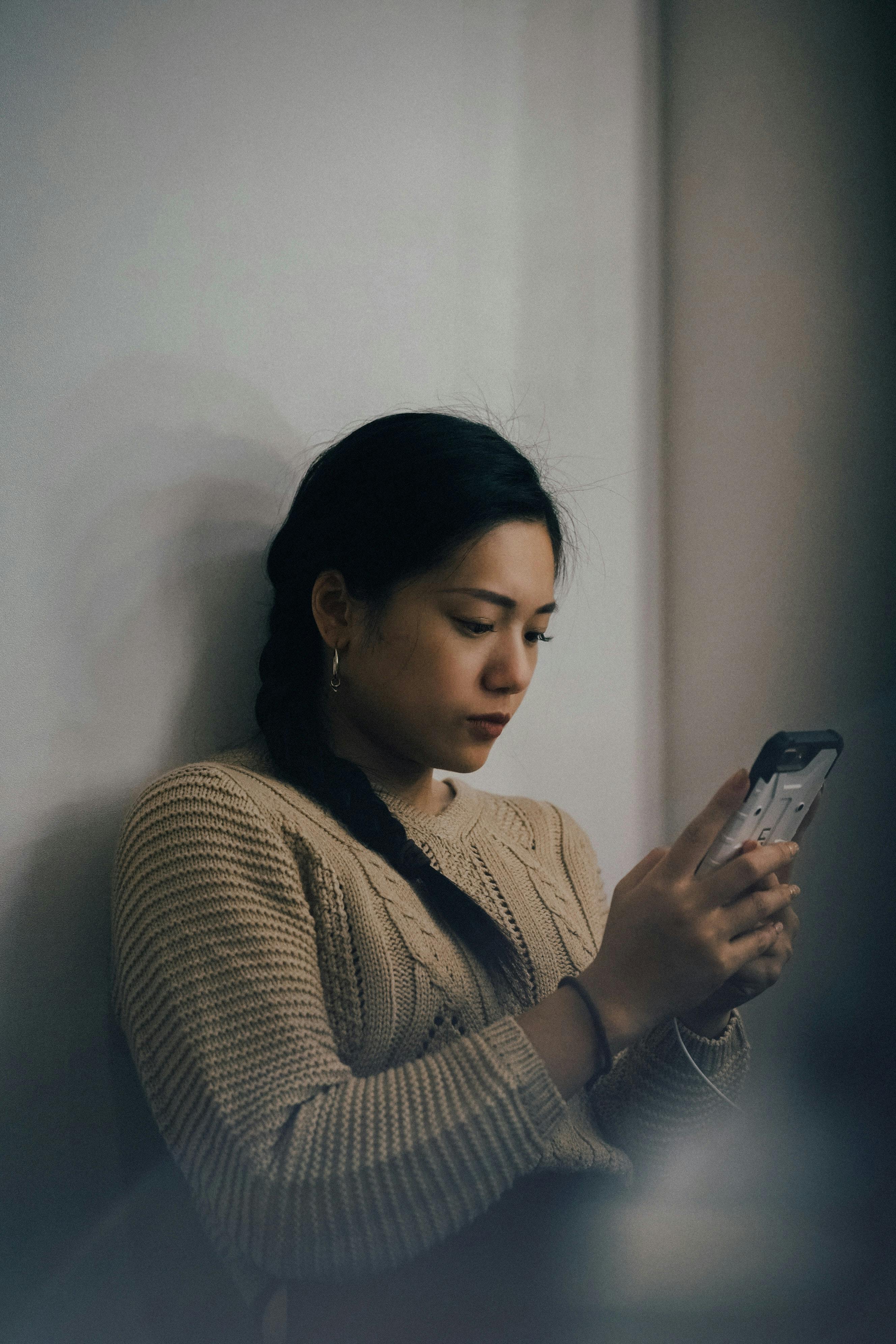 asian girl with black hair and grey sweater using an iphone