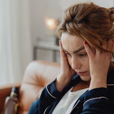 A stressed woman holding her temples, looking concerned while sitting at home, highlighting the mental and physical impact of stress on daily life.