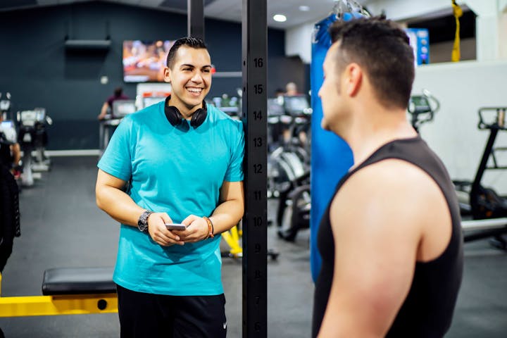 Two men-training in a gym, looking at a mobile phone