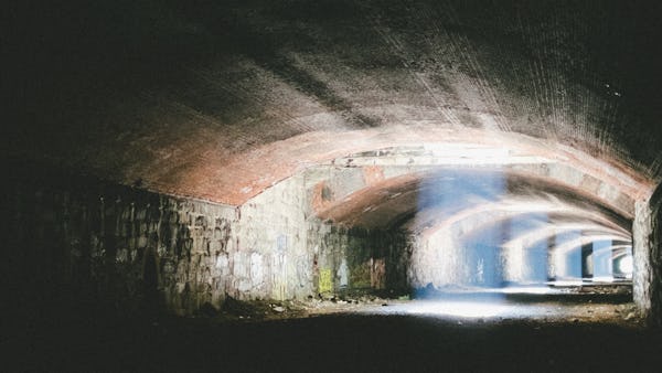 地下隧道的图像。光线从天花板的通风口射进来照亮砖墙和石墙