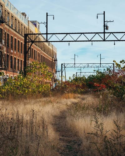 An image of the Viaduct. Brown grass grows on the ground, and a footpath is visble in the middle. A building presses up on the edge of the Viaduct to the left. The out of use metal train trestles remain on the structure.